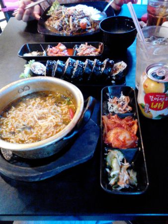 Whole set of ramyun, bulgogi, kimbab, side dish including kimchee, and peach juice..